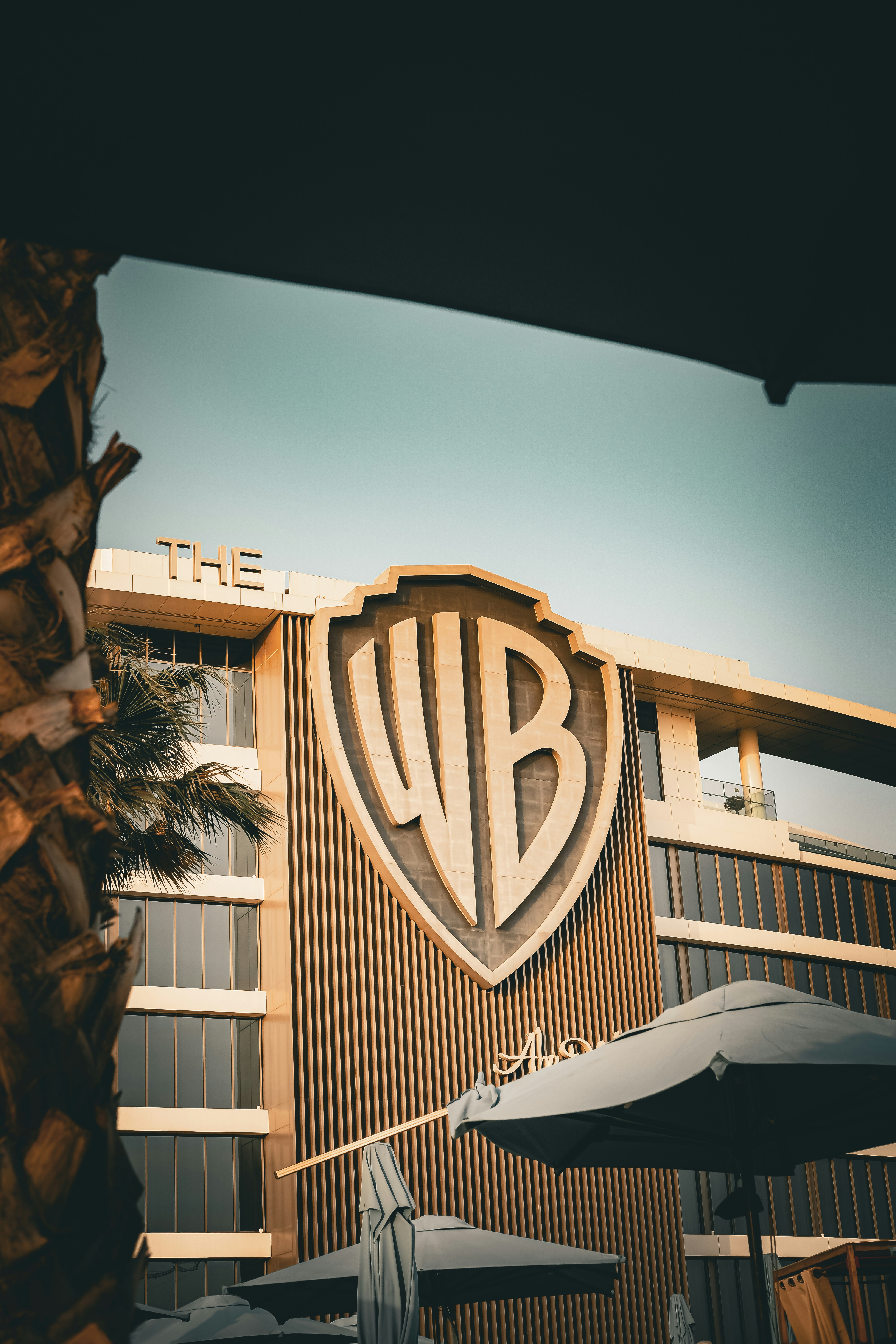 Budova Warner Bros s velkým logem na fasádě a slunečníky v popředí.